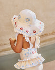 Child wearing a white sun hat and dress with floral patterns on a sandy background