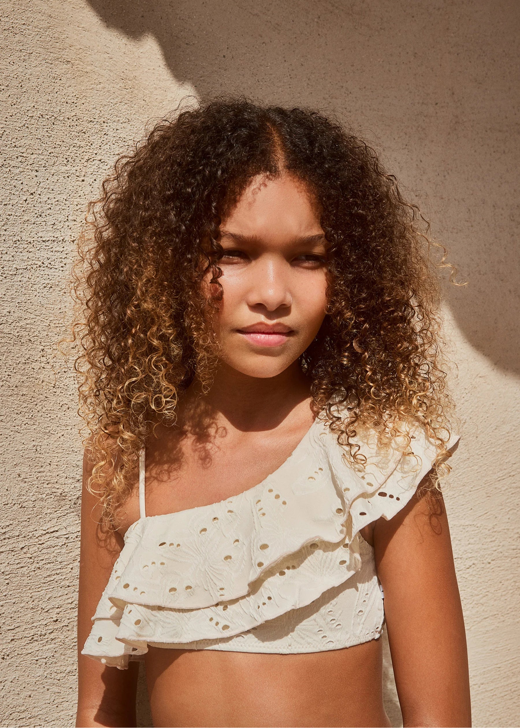 Woman wearing a white one-shoulder top against a beige wall