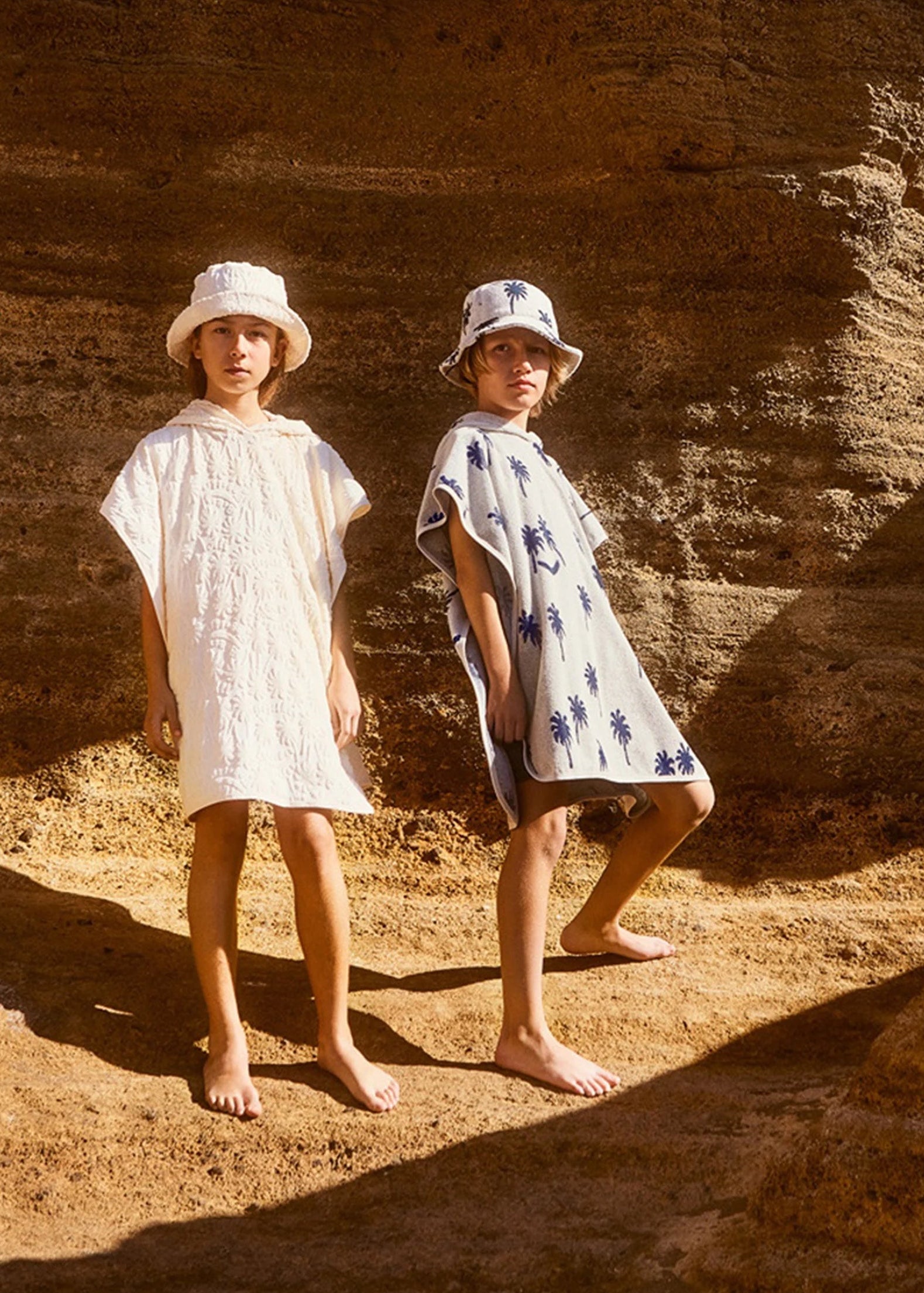 Two children in white dresses standing against a rocky wall.