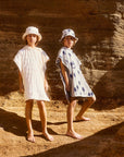 Two children in white dresses standing against a rocky wall.