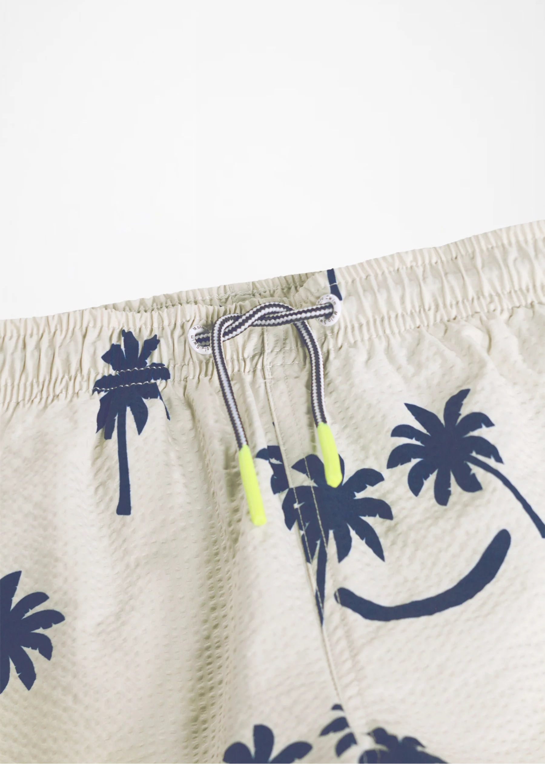 Beige swim shorts with navy palm tree pattern on a white background