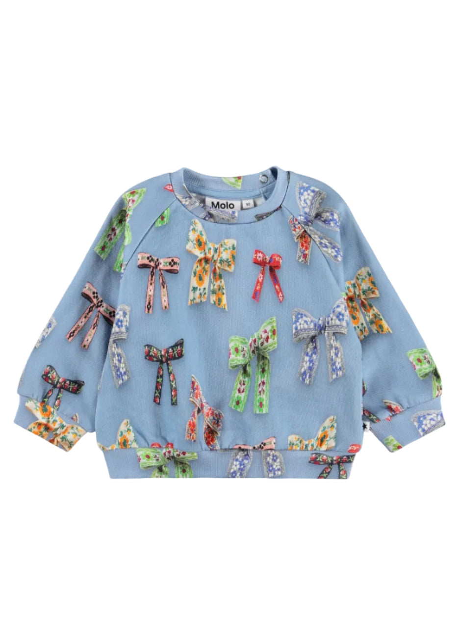 A light blue long-sleeve sweatshirt for children, featuring an all-over print of colorful bow and ribbon motifs in various patterns, shown flat against a white background.