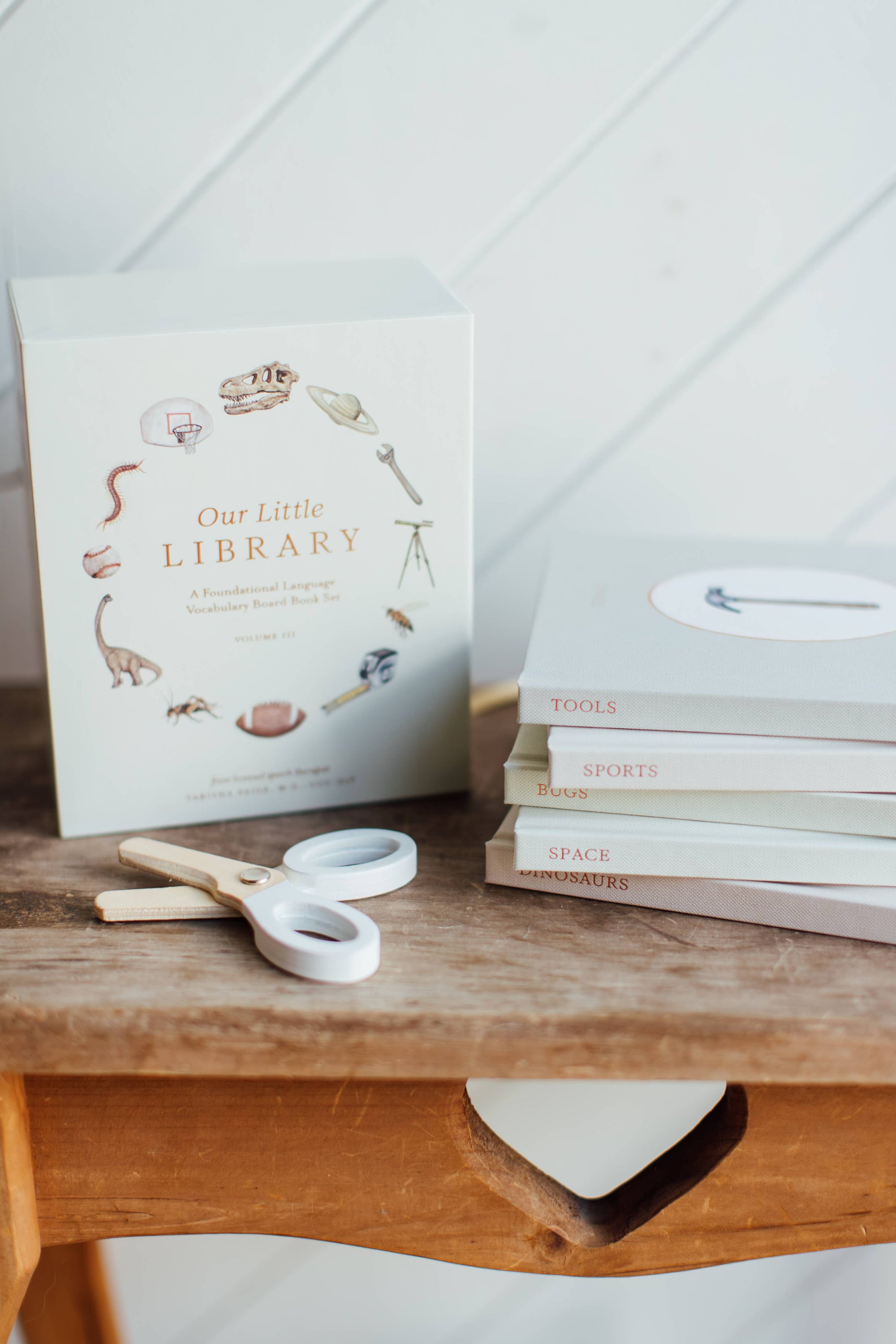 Stack of books titled 'Our Little Library' on a wooden surface with a white background
