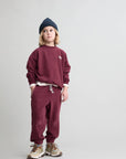 Child wearing a maroon sweatshirt and pants with a beanie on a light gray background