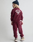 Child wearing a maroon tracksuit with 'Tennis Camp' text on the back against a plain background