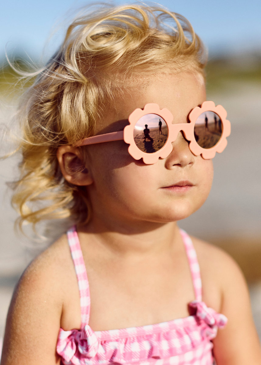Young girl wearing pink sunglasses and a pink dress on a beach.