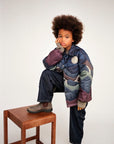 Child wearing a colorful puffer jacket sitting on a wooden stool against a white background
