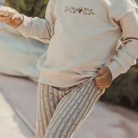 Child wearing a beige sweatshirt with a floral design and patterned pants outdoors.