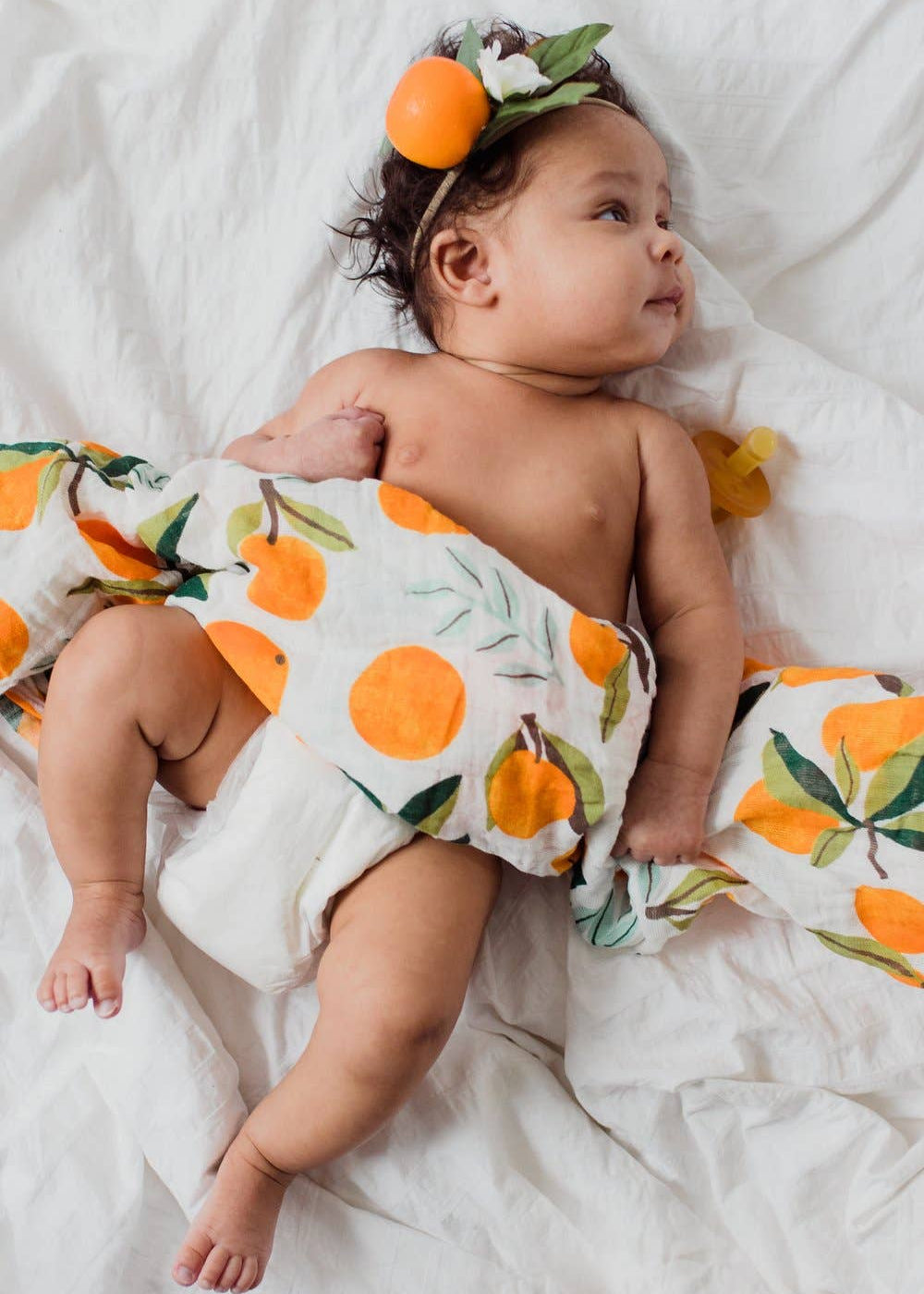 Baby wrapped in a cloth with orange pattern on a white blanket