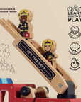Wooden toy fire station with firefighters and a retractable ladder on a beige background.