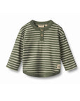 A toddler's long-sleeve henley shirt in olive green and cream stripes, featuring a three-button placket and a small embroidered patch on the lower left hem, shown against a plain white background.