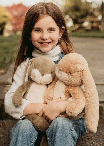 Young girl holding two plush bunnies in a park setting