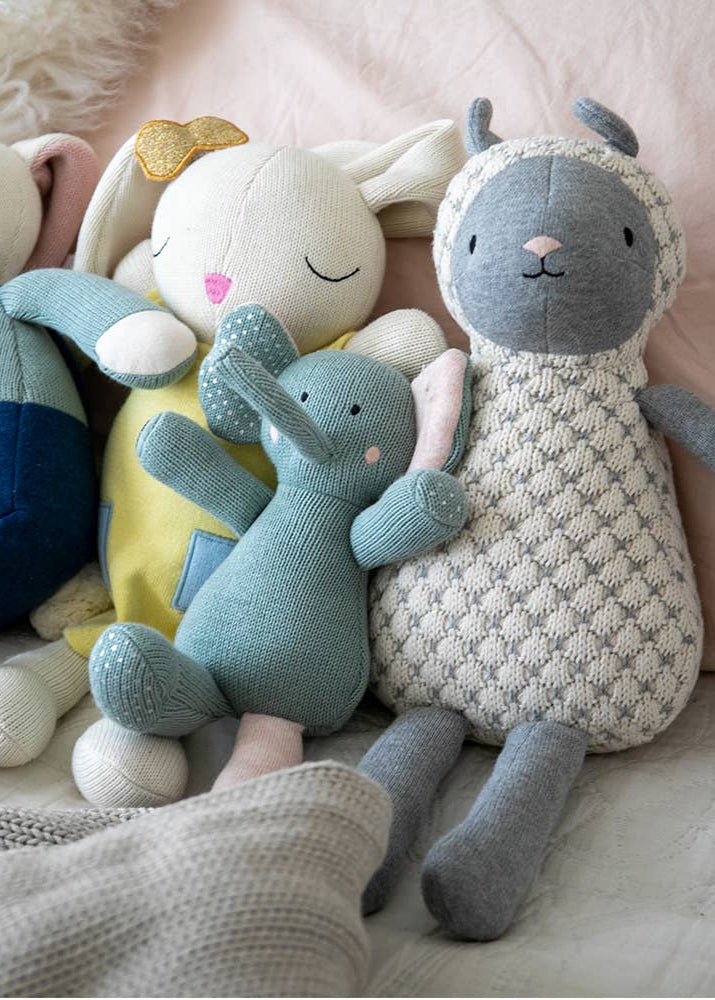 Four soft toys, including a rabbit, bear, elephant, and sheep, sitting together on a textured surface.