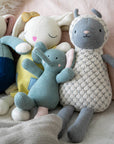 Four soft toys, including a rabbit, bear, elephant, and sheep, sitting together on a textured surface.