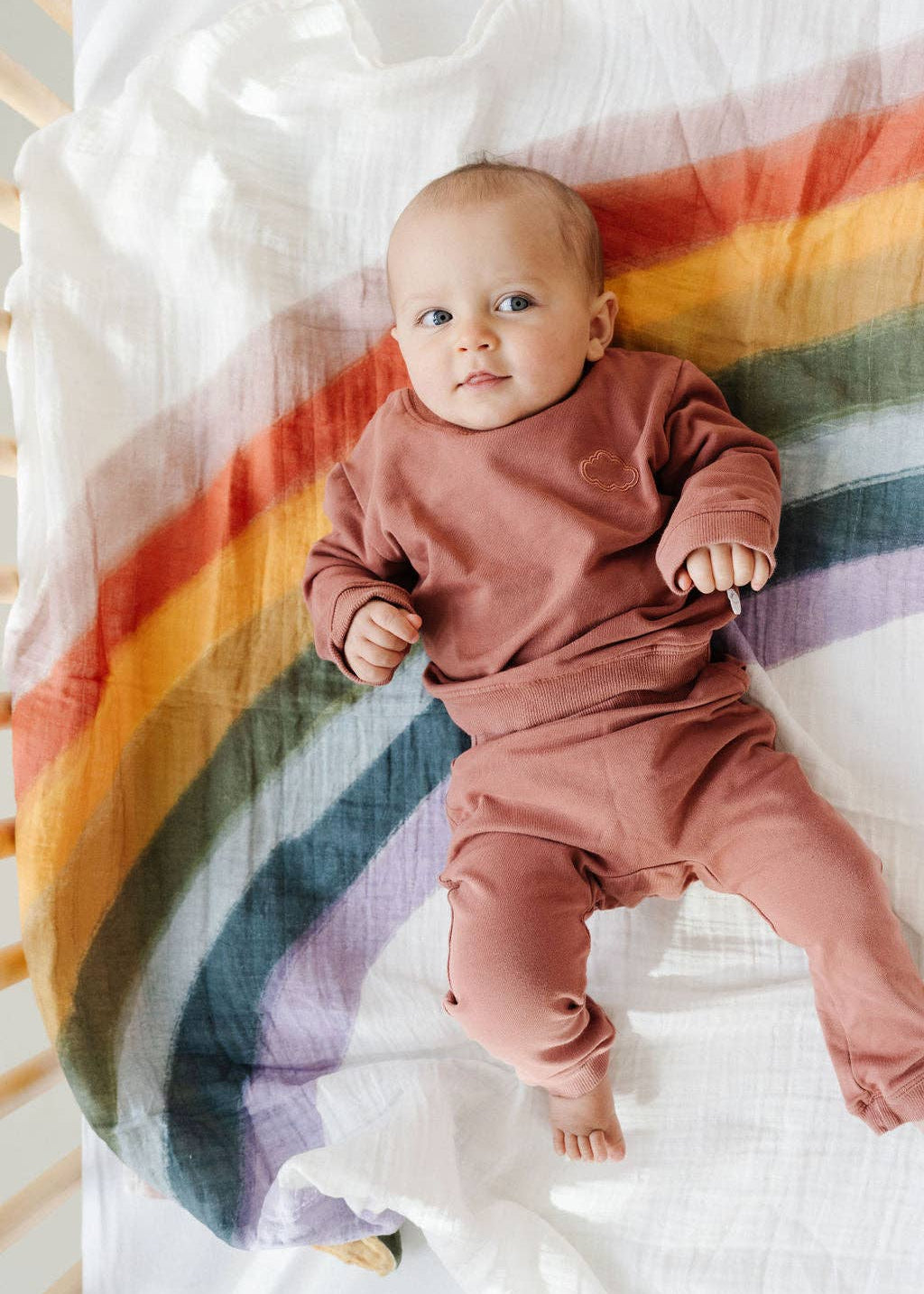 Baby in pink outfit lying on a rainbow-patterned blanket