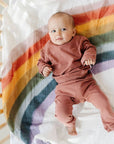 Baby in pink outfit lying on a rainbow-patterned blanket