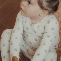 Child wearing a light-colored outfit with a subtle pattern, sitting on a wooden floor.