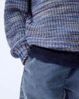 Close-up of a person wearing a blue and gray patterned sweater and blue pants on a white background