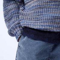 Close-up of a person wearing a blue and gray patterned sweater and blue pants on a white background