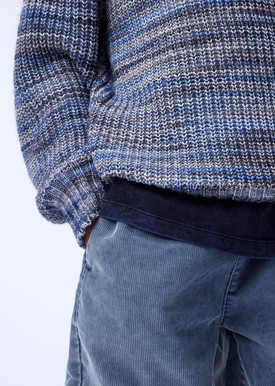 Close-up of a person wearing a blue and gray patterned sweater and blue pants on a white background
