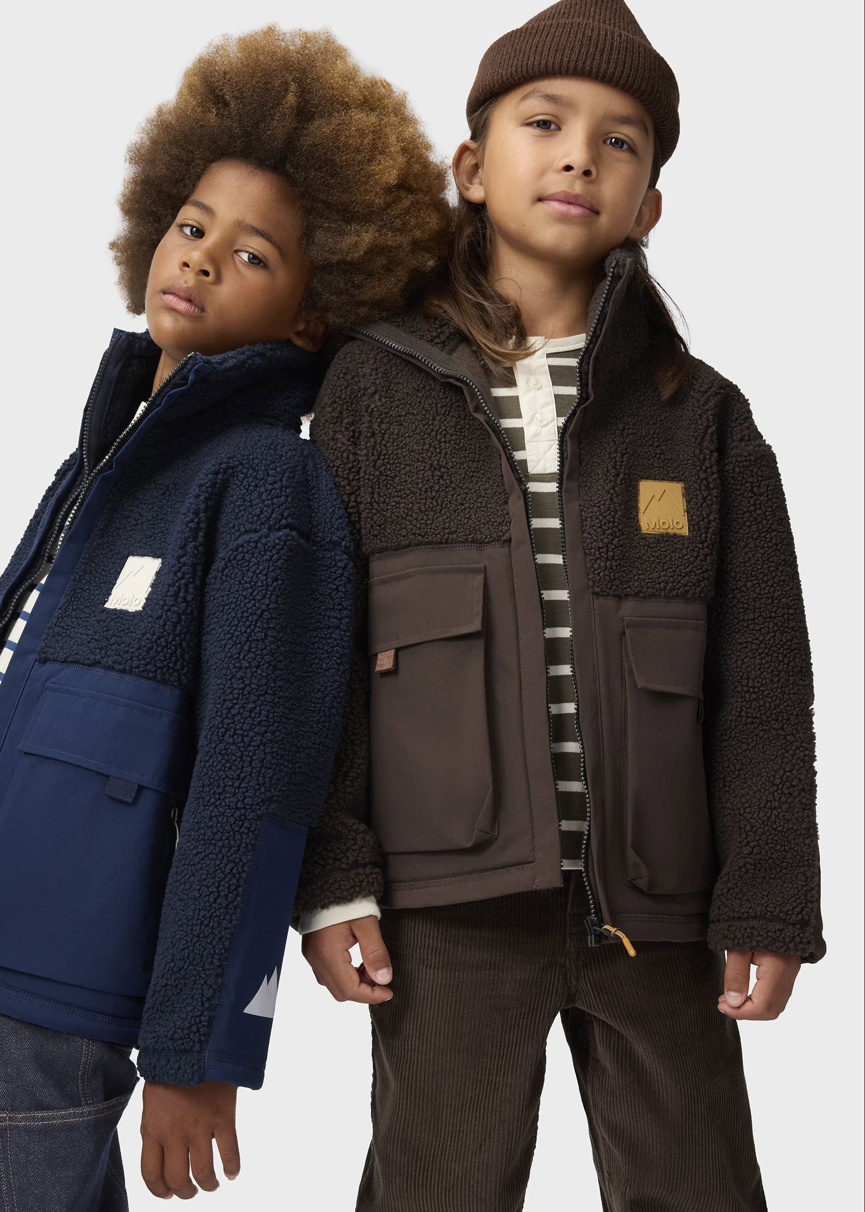 Two children wearing jackets standing side by side against a white background