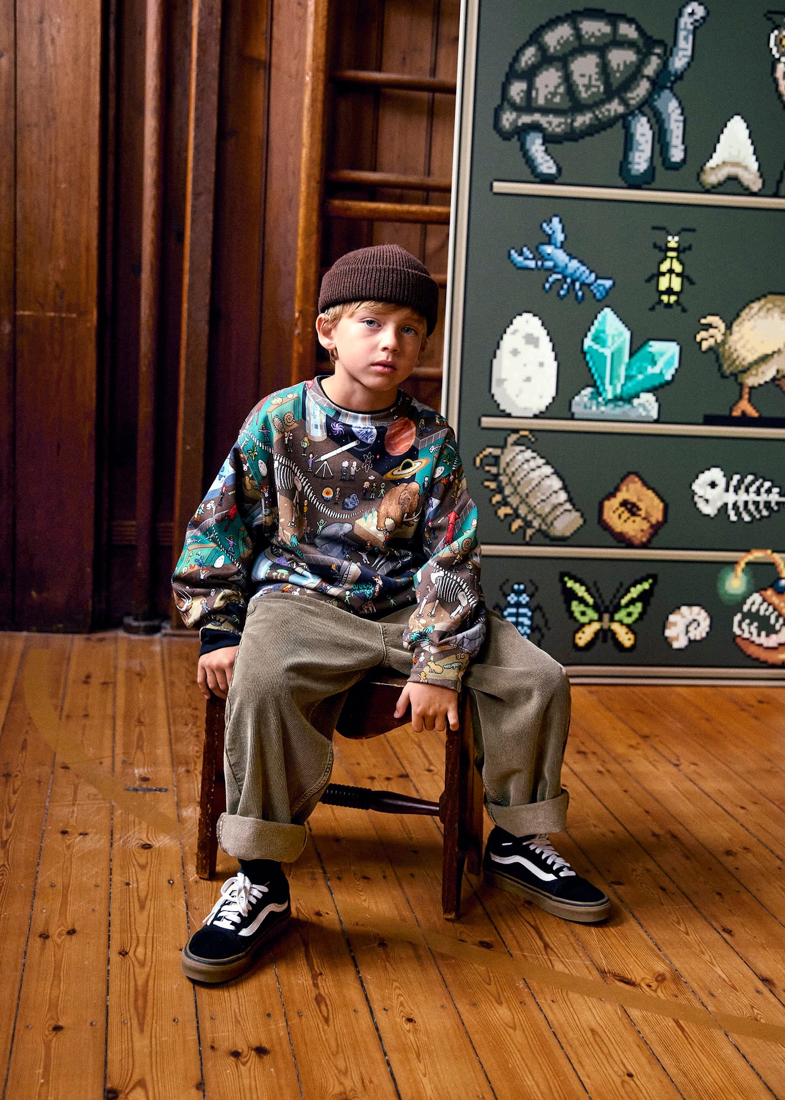 Child sitting on a chair in front of a chalkboard with educational drawings.