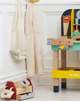 Children's toy workbench with tools and a toolbox on a white floor.