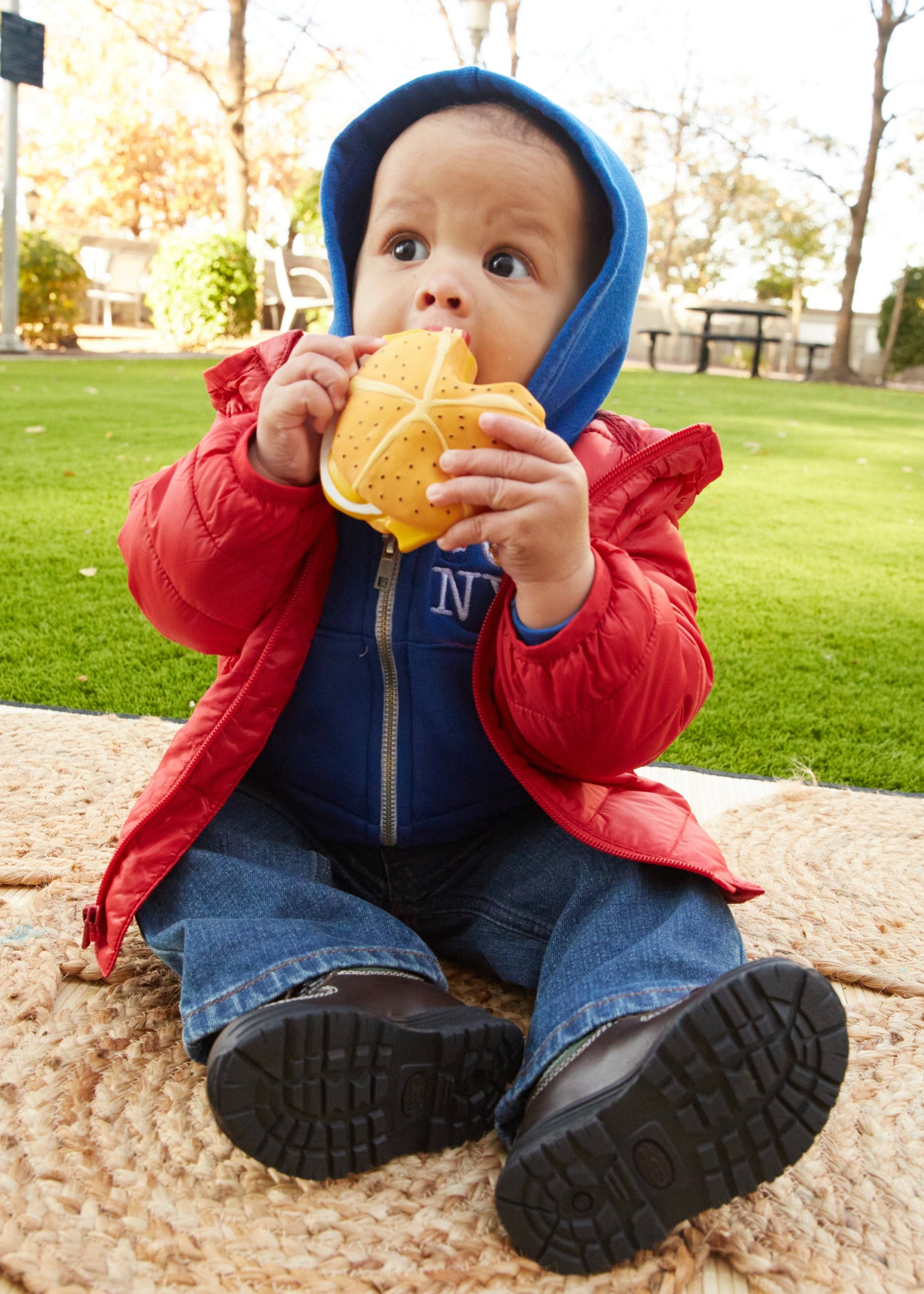 Child in a red and blue jacket eating a sandwich outdoors