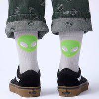 White socks with green alien faces worn by a person with black shoes on a white background