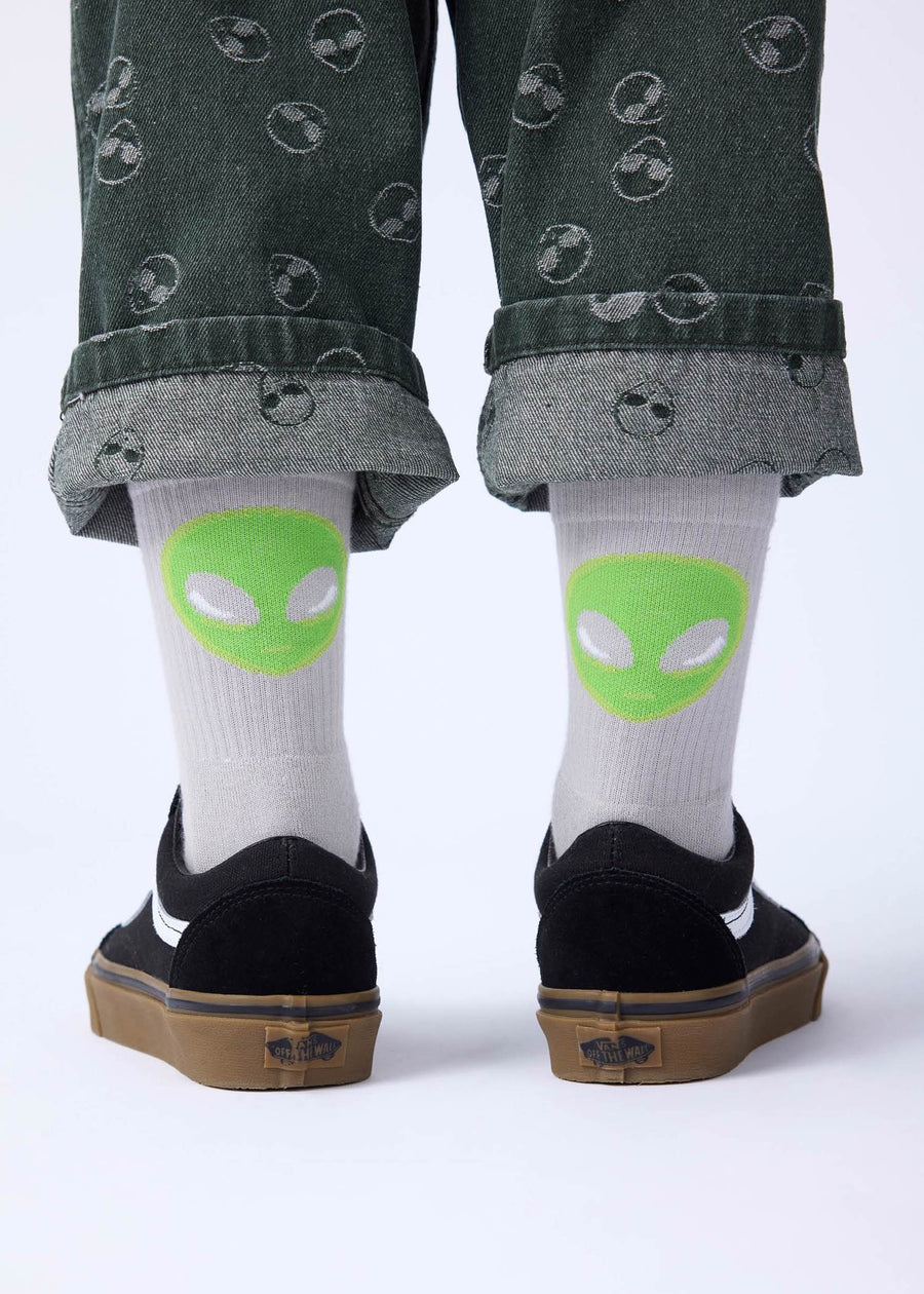 White socks with green alien faces worn by a person with black shoes on a white background