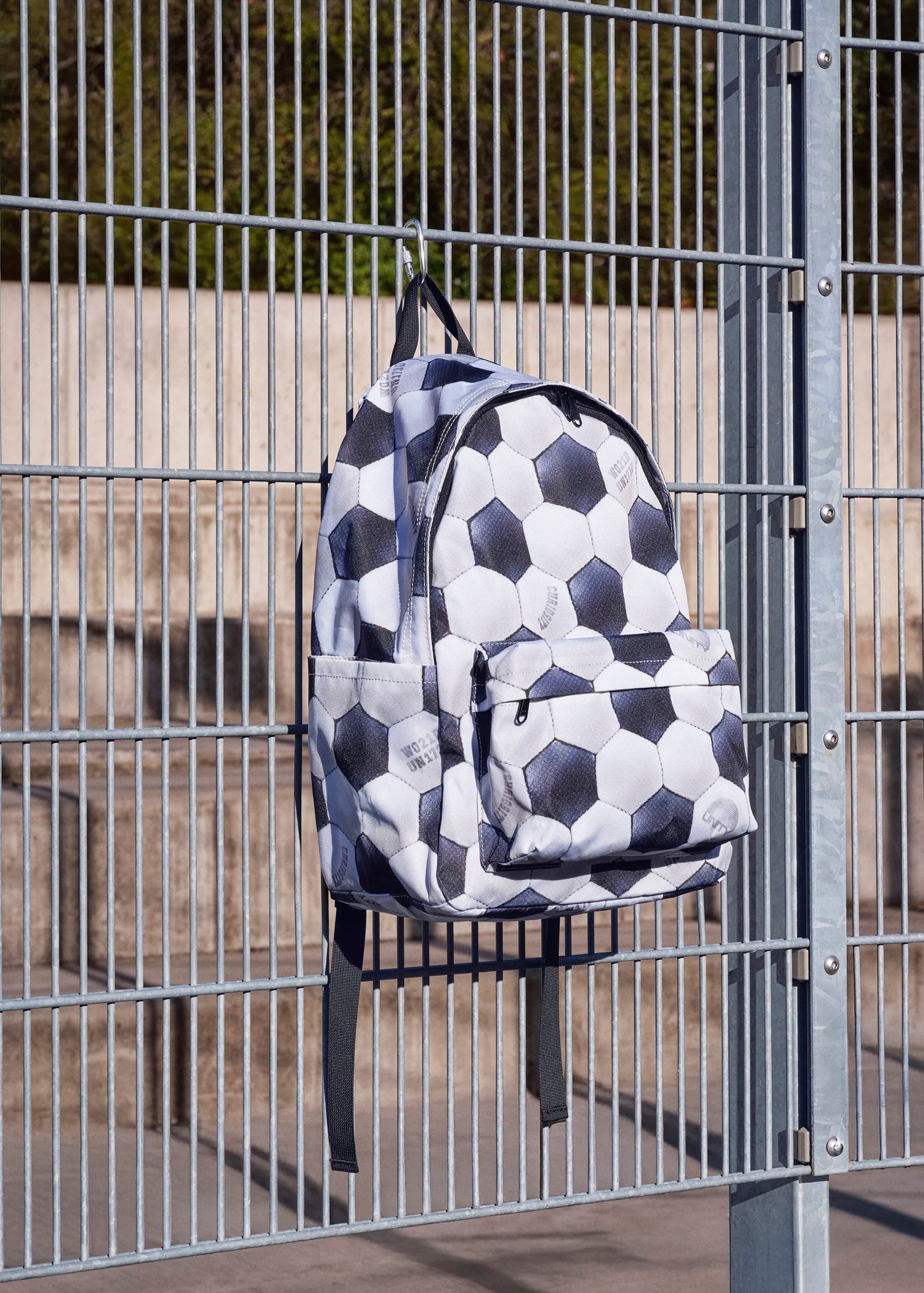 Backpack with soccer ball pattern hanging on a metal fence