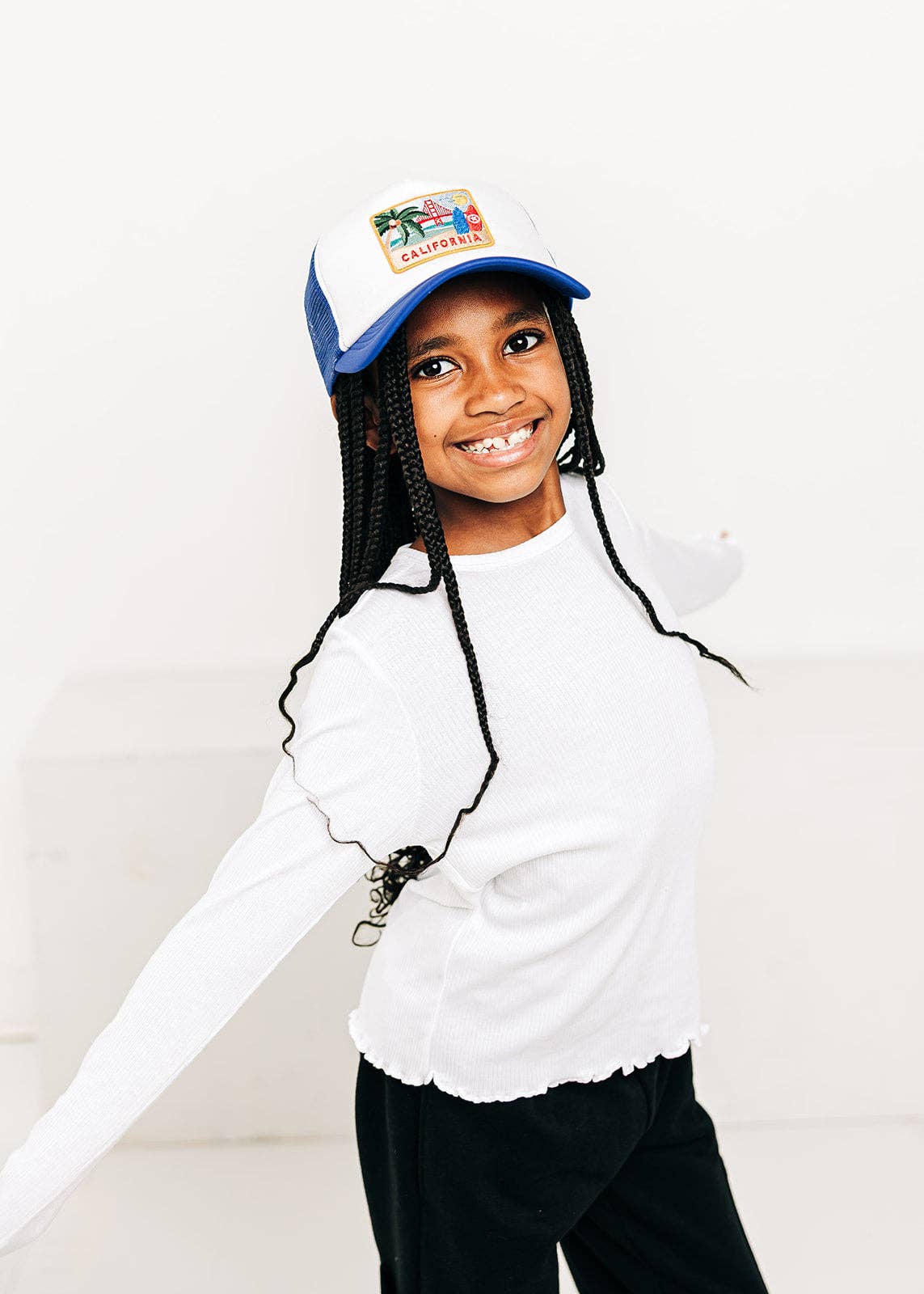 Child wearing a white long-sleeve shirt and black pants with a blue cap on a white background