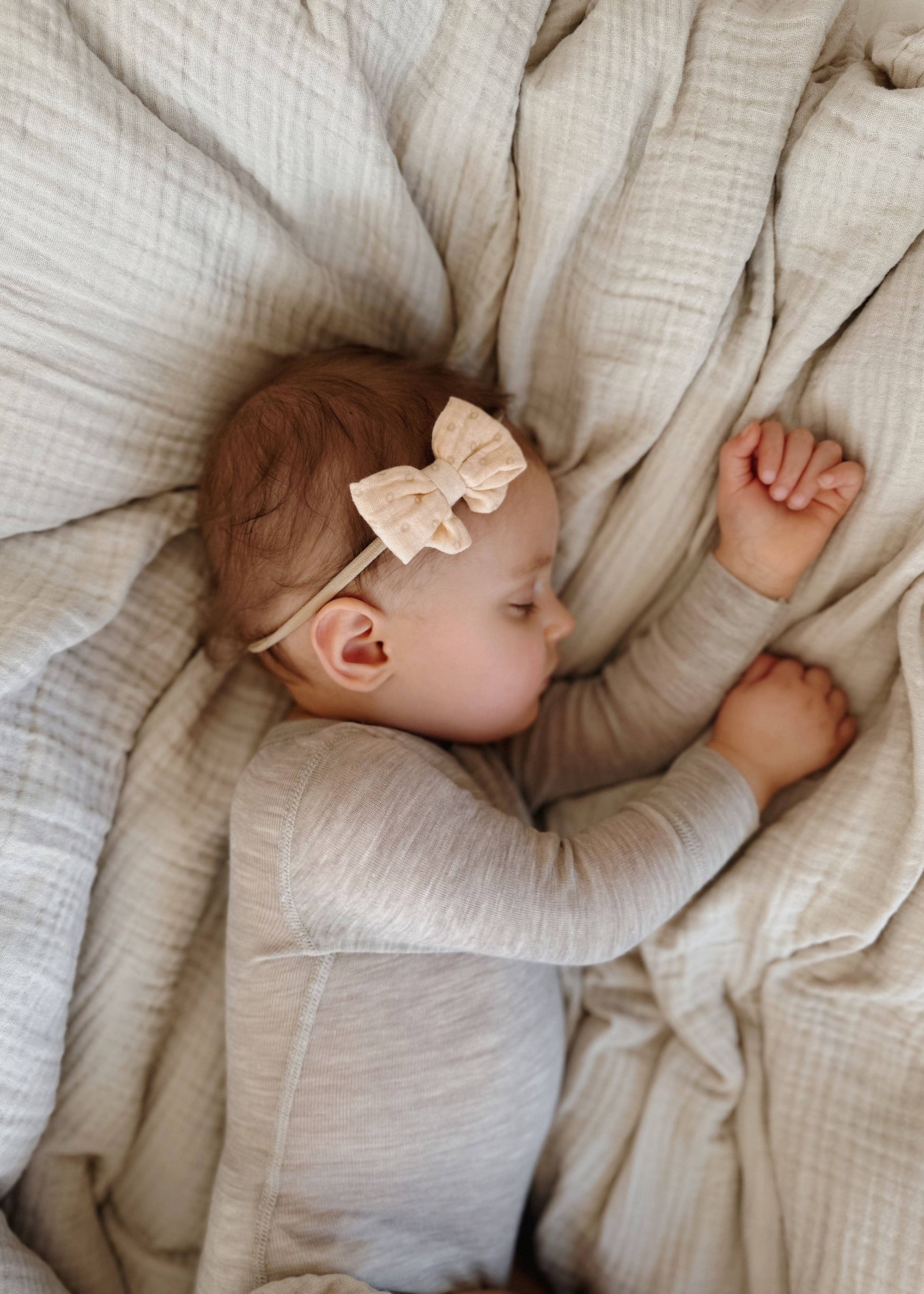 Baby lying on a soft blanket wearing a beige bow headband.