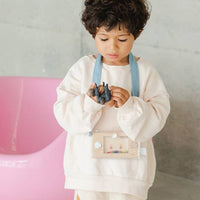 Child in a white outfit standing on a colorful rug with a pink chair in the background