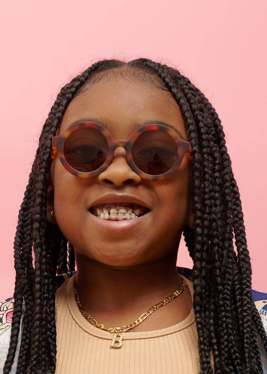Young girl with braided hair wearing sunglasses against a pink background