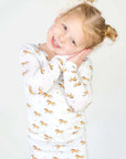 Child wrapped in a white blanket with gold animal patterns on a plain background
