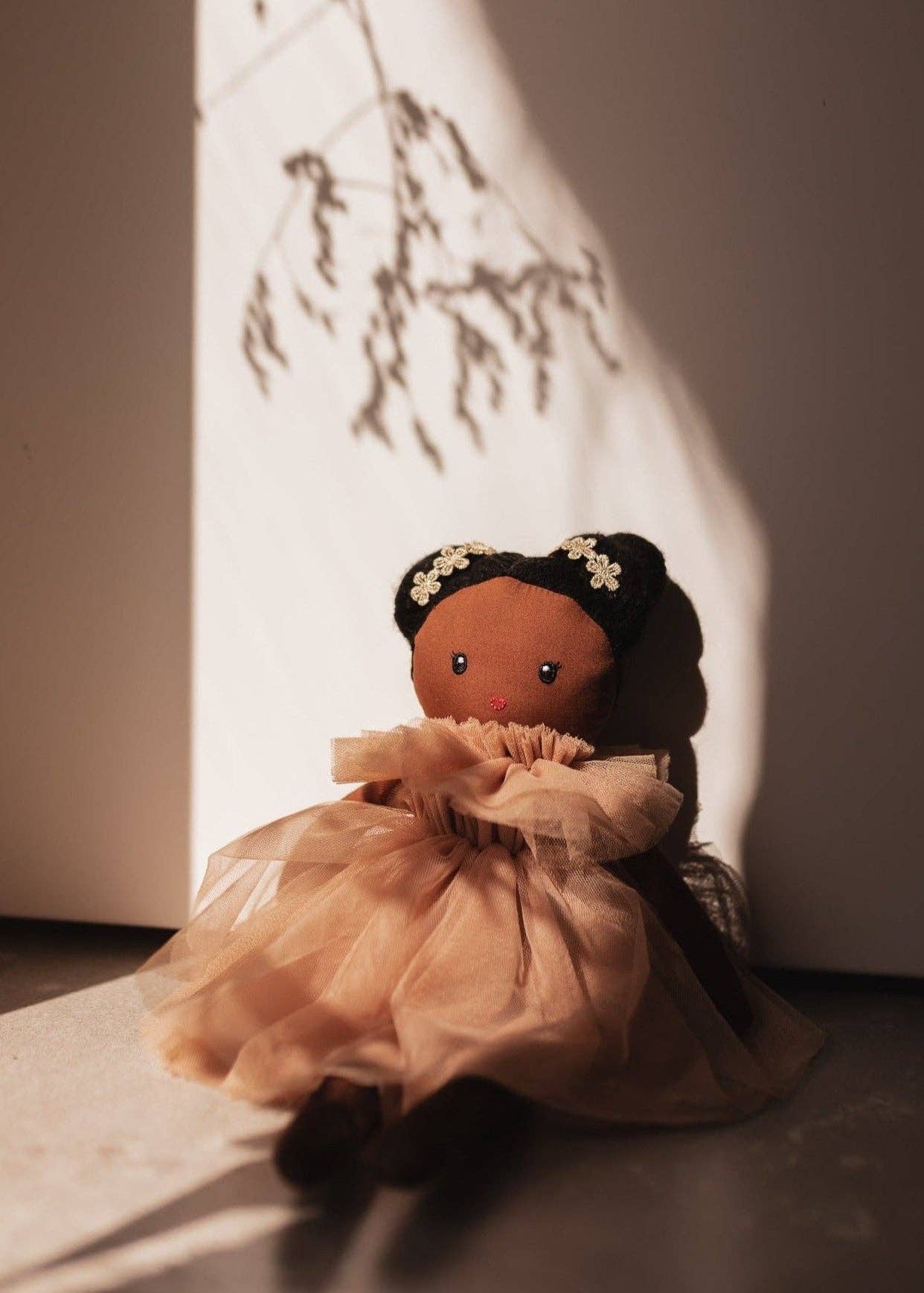 Textile doll with dark hair and a beige dress in soft lighting