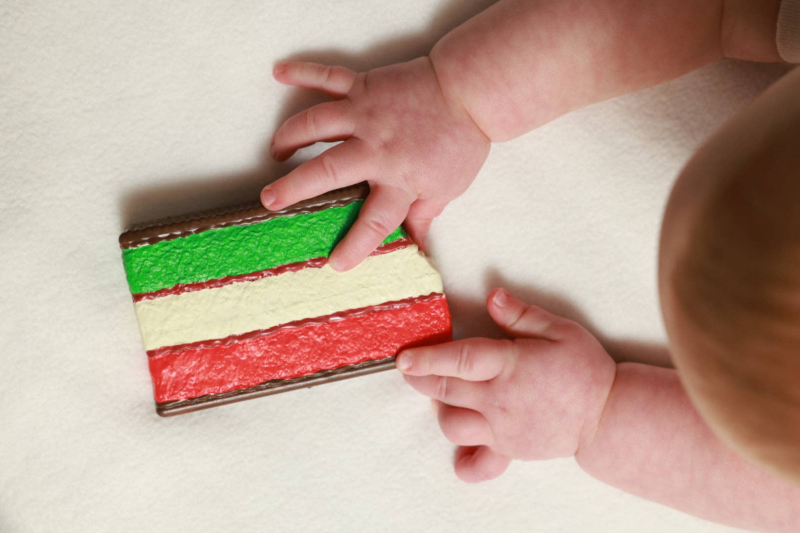 Baby's hands reaching towards a colorful striped block on a light surface
