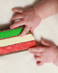 Baby's hands reaching towards a colorful striped block on a light surface