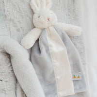 Fluffy white rabbit plush toy with a gray scarf on a soft gray background