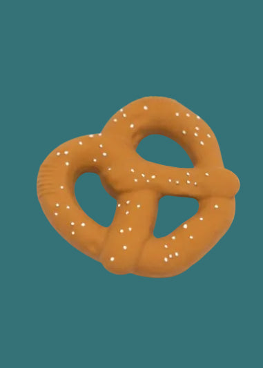 A novelty pretzel-shaped dog toy in a warm brownish-orange color with white faux-seed details, set against a solid teal background.