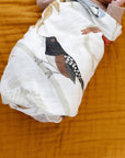 Baby wrapped in a white blanket with a bird design on a mustard yellow background