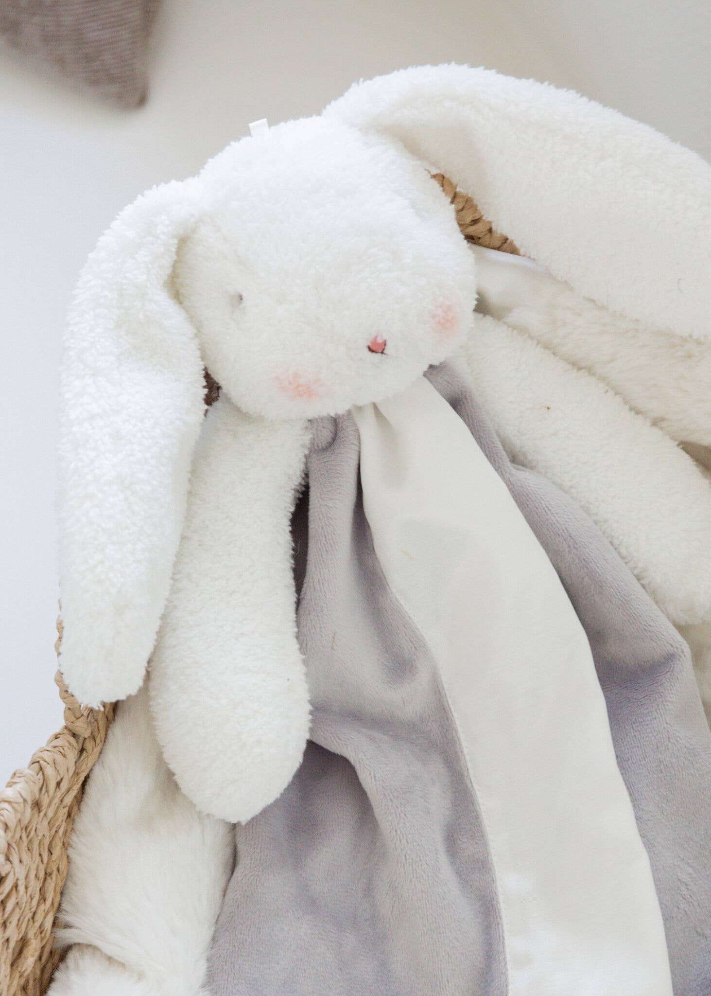 White plush bunny toy with a soft blanket in a woven basket