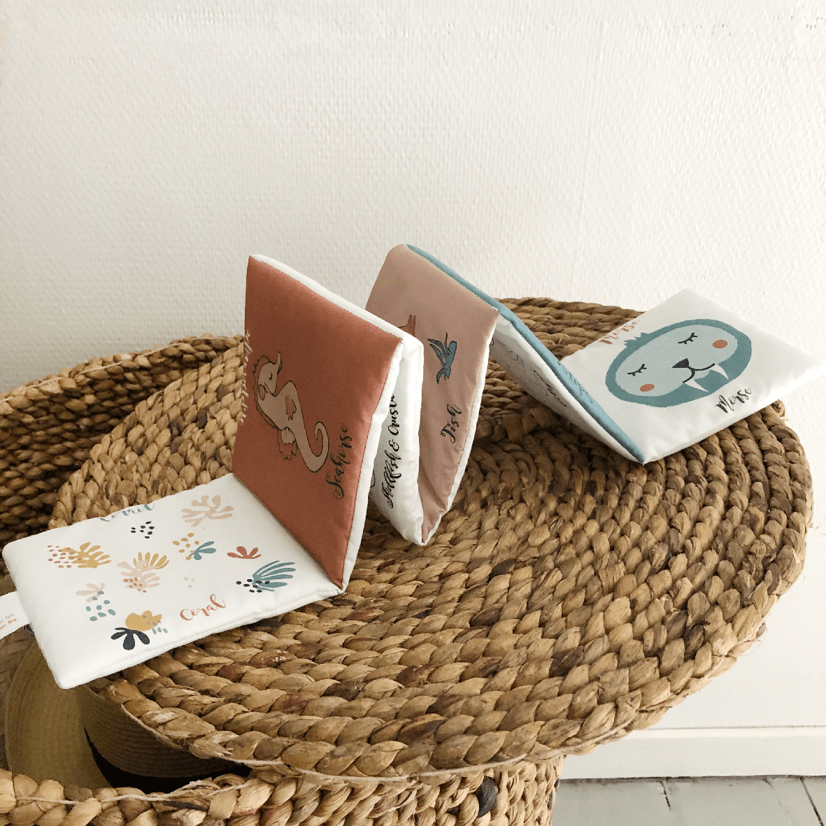 Four small books with animal illustrations on a woven mat.