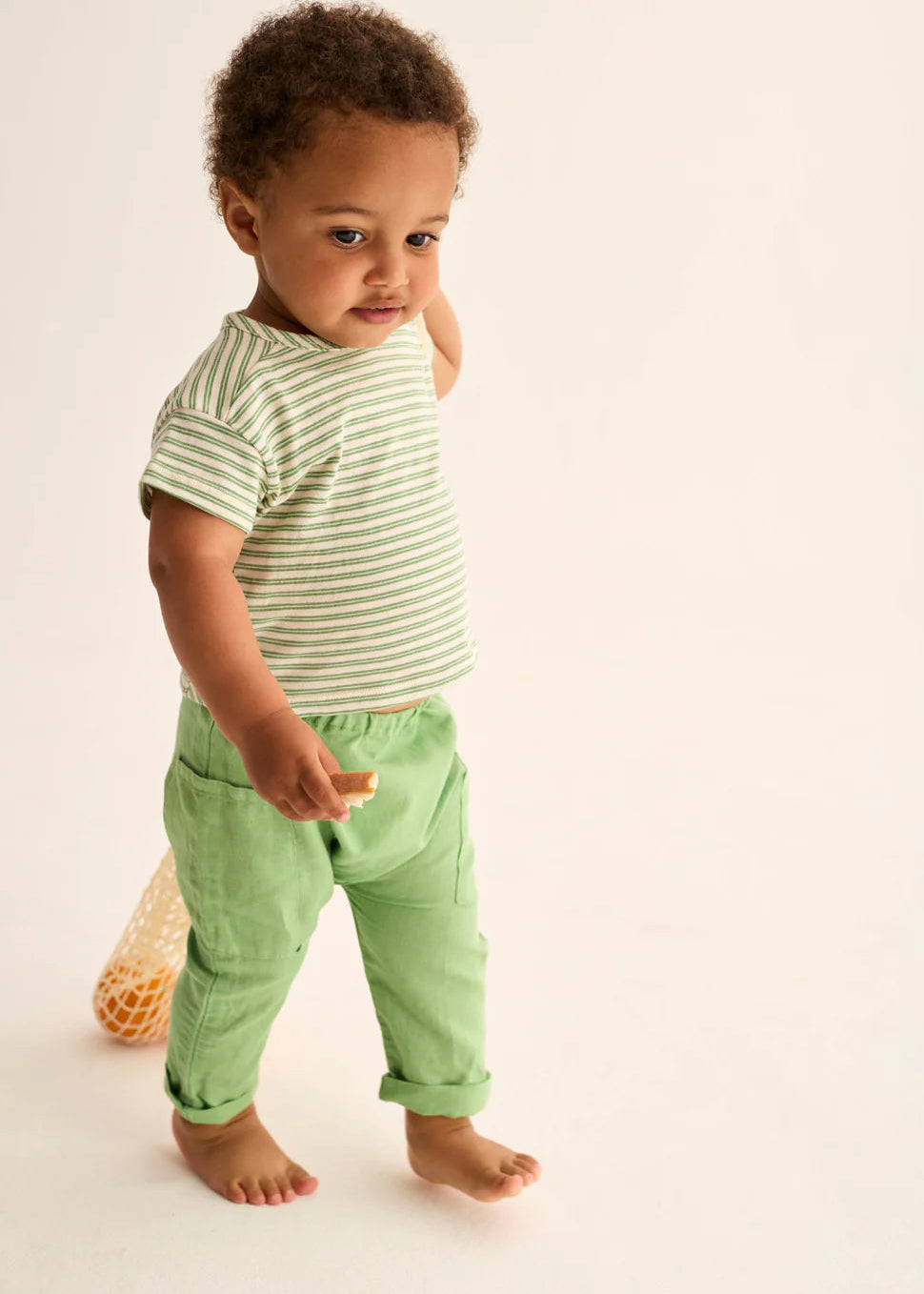 Child wearing a green and white striped shirt and green pants on a plain background