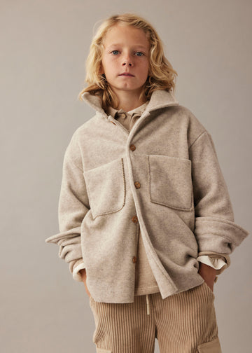 Person wearing a beige coat and cargo pants against a plain background