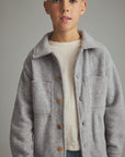 A young boy wearing a light gray wool-blend button-up jacket over a cream t-shirt, photographed against a solid gray studio background.
