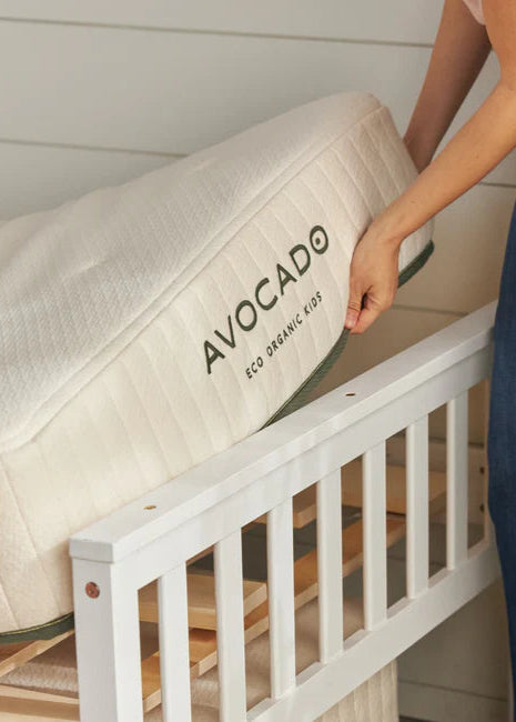Person placing an Avocado eco organic crib mattress on a white crib.
