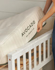 Person placing an Avocado eco organic crib mattress on a white crib.