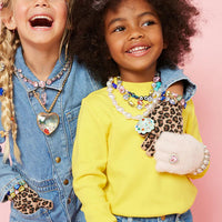 Two children wearing colorful jewelry against a pink background